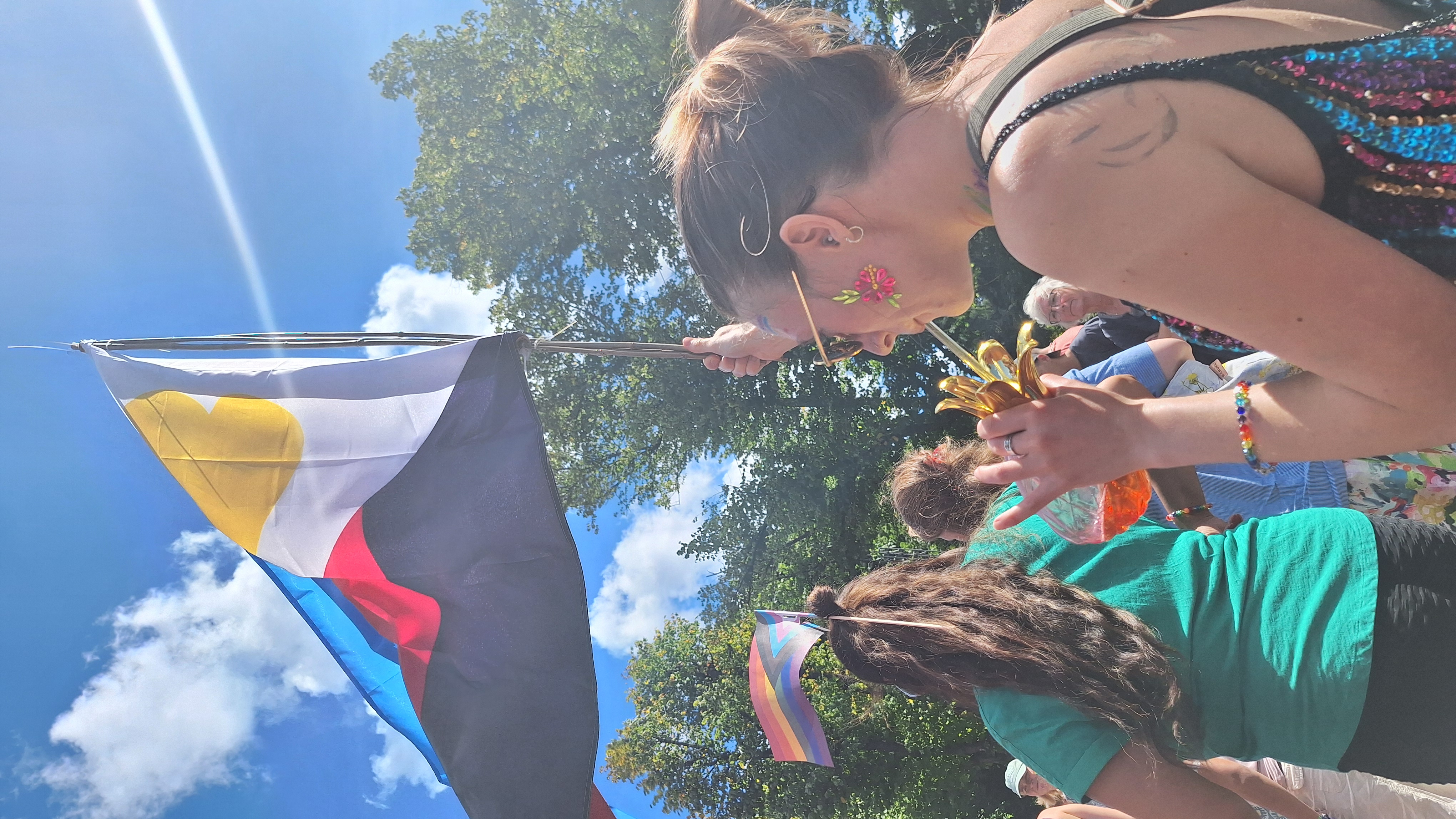 Kvinde holder polyamori-flag højt ved Pride-march i solskin